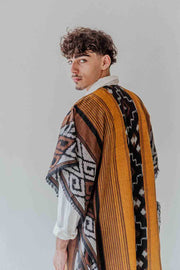 Man wearing a patterned shawl over a white shirt against a plain background