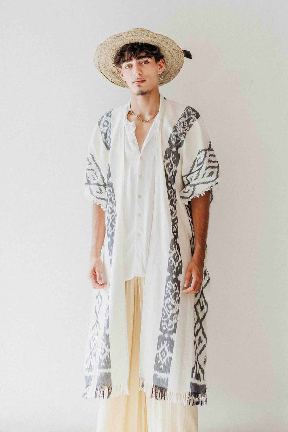 Person wearing a long, patterned kimono-style garment with a straw hat on a plain background