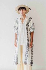 Person wearing a long, patterned kimono-style garment with a straw hat on a plain background