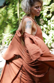 Woman wearing a flowing rust-colored dress with a blurred natural background