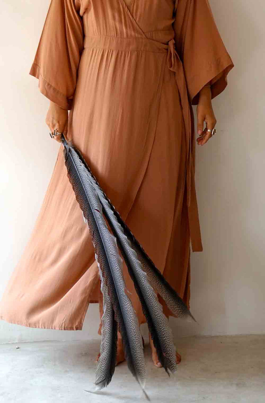 Person wearing a brown dress holding a long, dark fabric against a plain background