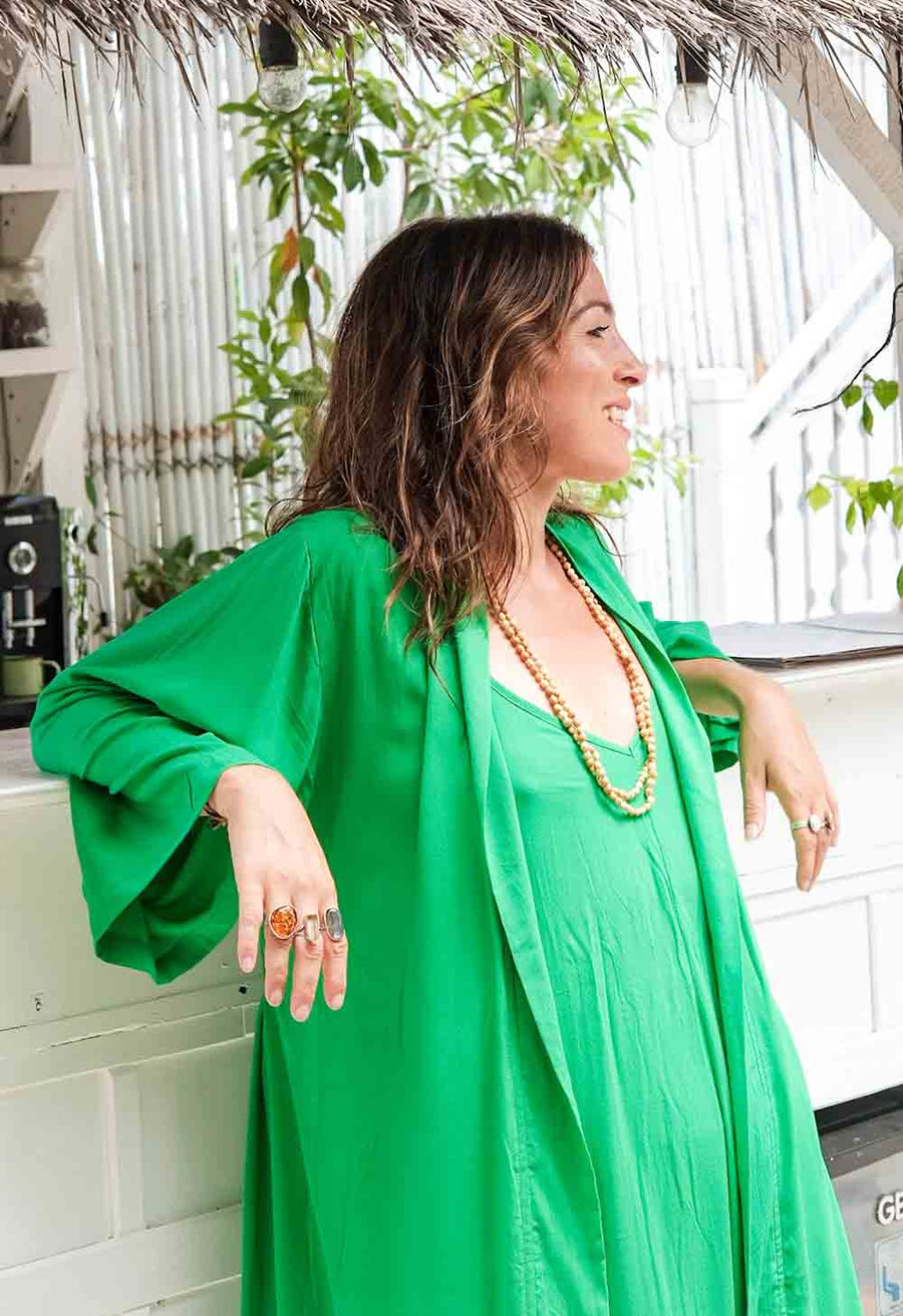 Woman in a green dress with a necklace, sitting outdoors with plants in the background