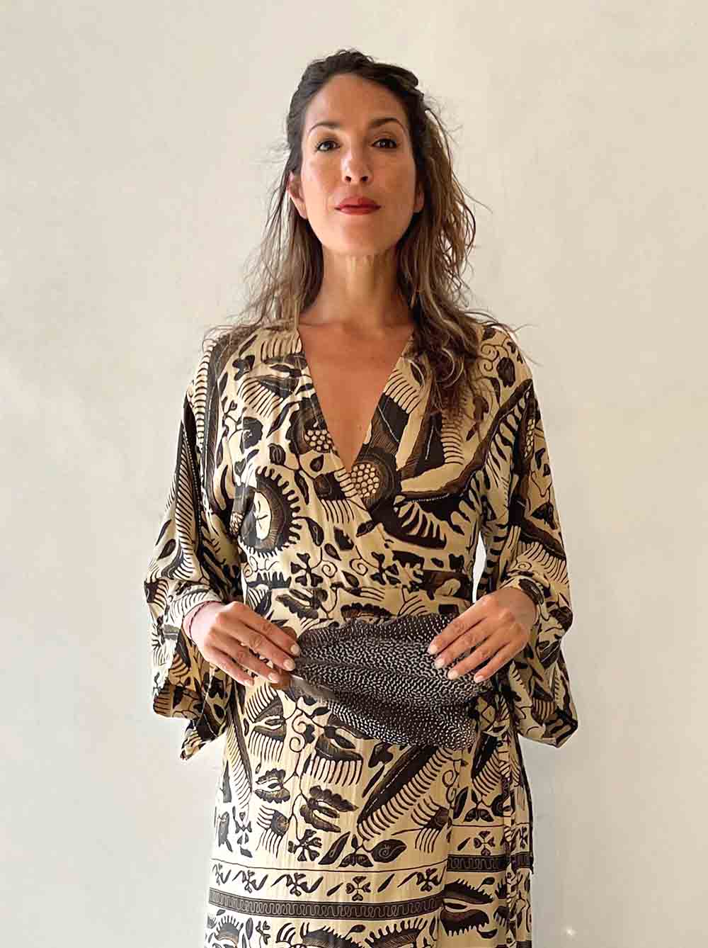 Woman wearing a patterned dress holding a handbag against a plain background