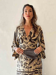 Woman wearing a patterned dress holding a handbag against a plain background