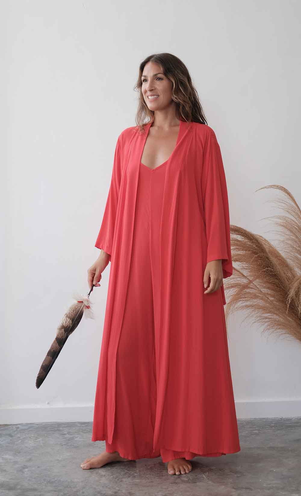 Woman wearing a coral long dress holding a feathered object against a white wall.