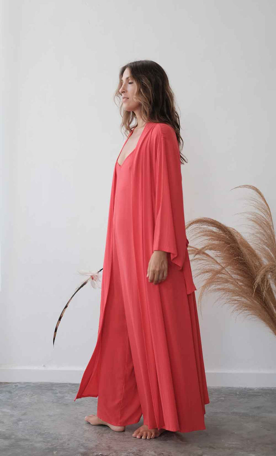 Woman wearing a coral-colored dress standing against a white wall with decorative elements.