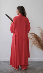 Person wearing a red outfit holding a black object against a white wall with decorative plants.
