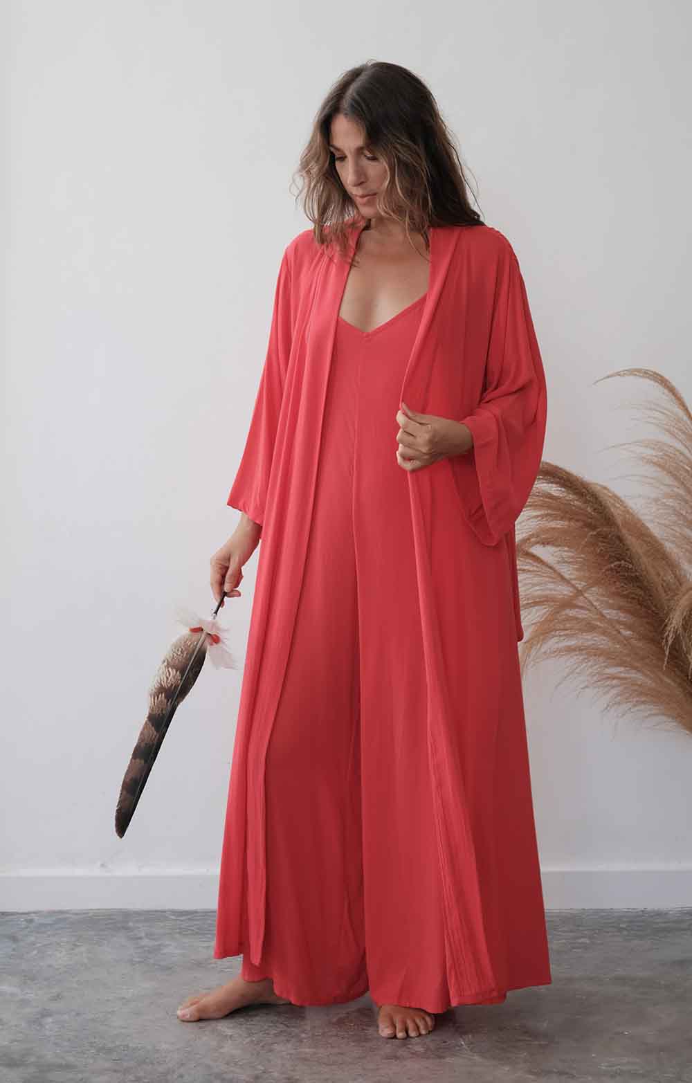 Woman in a long red robe holding a feather duster against a white wall.
