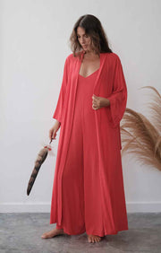 Woman in a long red robe holding a feather duster against a white wall.