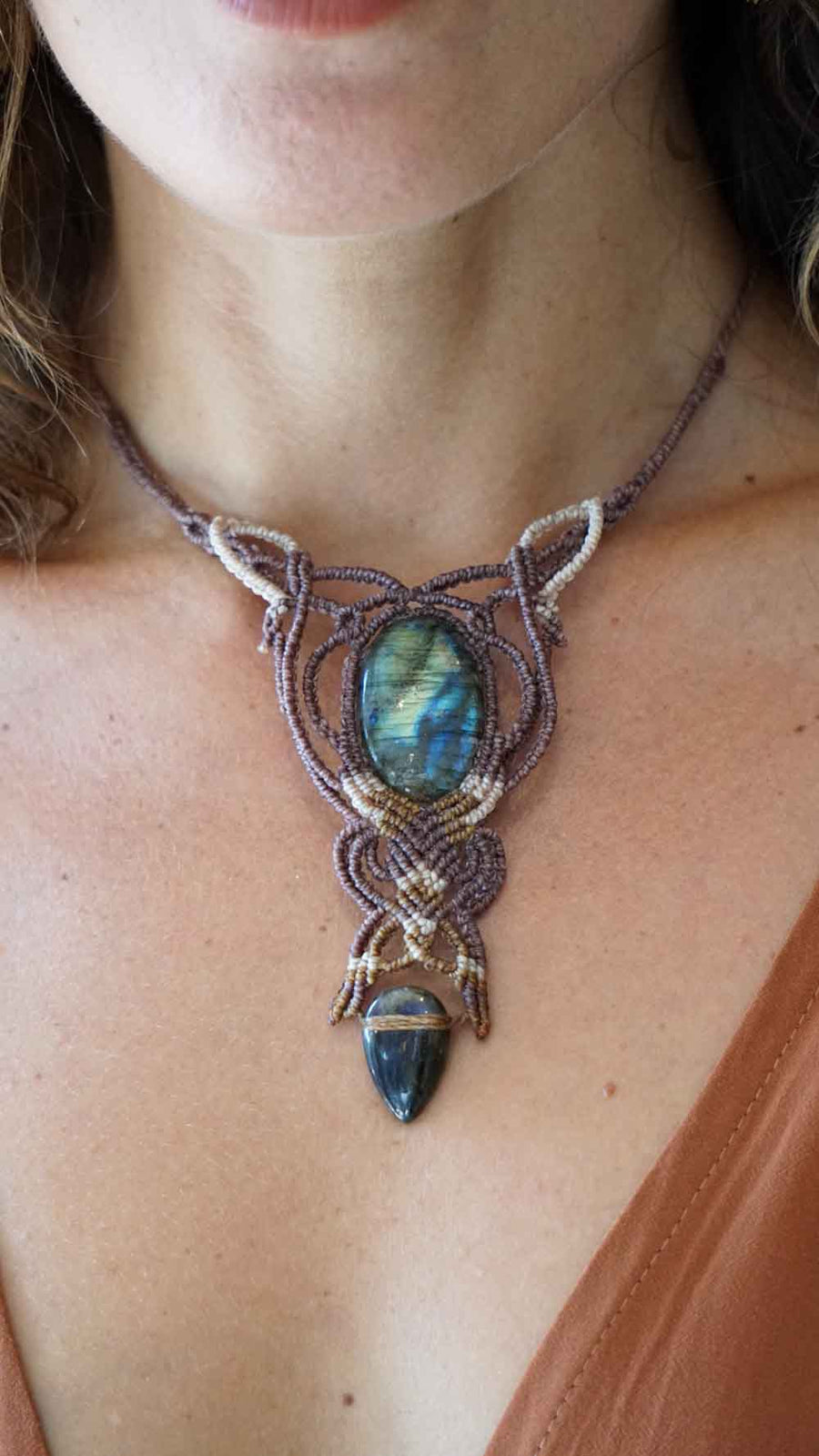 Close-up of a macrame necklace with a Labradorite stone pendant on a person.