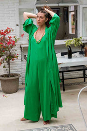 Woman wearing a green dress standing outdoors with a white building and plants in the background