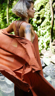 Person wearing a rust-colored outfit standing in a natural setting with greenery.