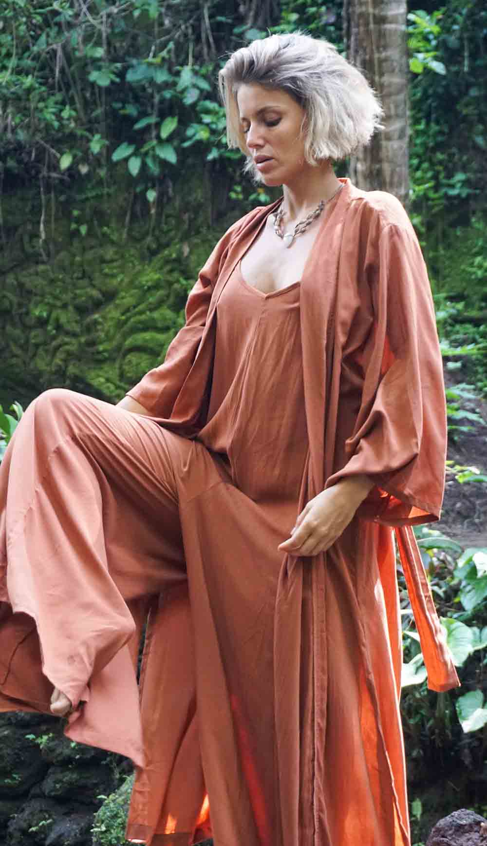 Woman in a peach-colored outfit sitting in a natural setting with greenery.
