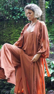 Woman in a peach-colored outfit sitting in a natural setting with greenery.