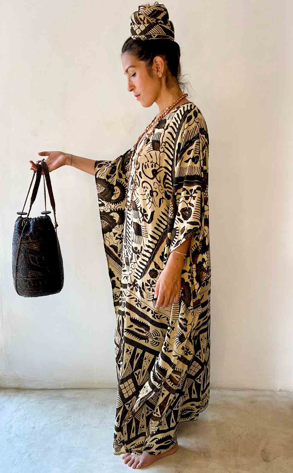 Woman wearing a patterned dress holding a black bag against a white background