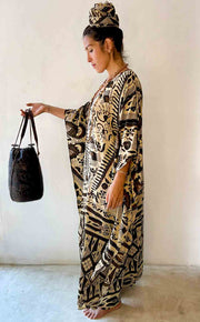 Woman wearing a patterned dress holding a black bag against a white background