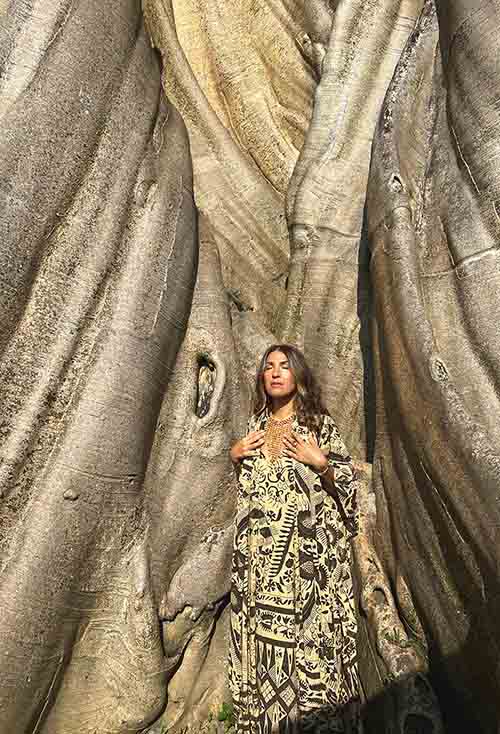 Woman standing inside a large tree with intricate patterns on its bark