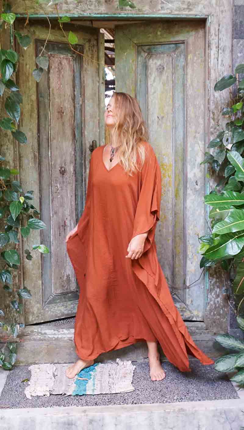 Woman in a rust-colored dress standing in front of a wooden door with greenery around.