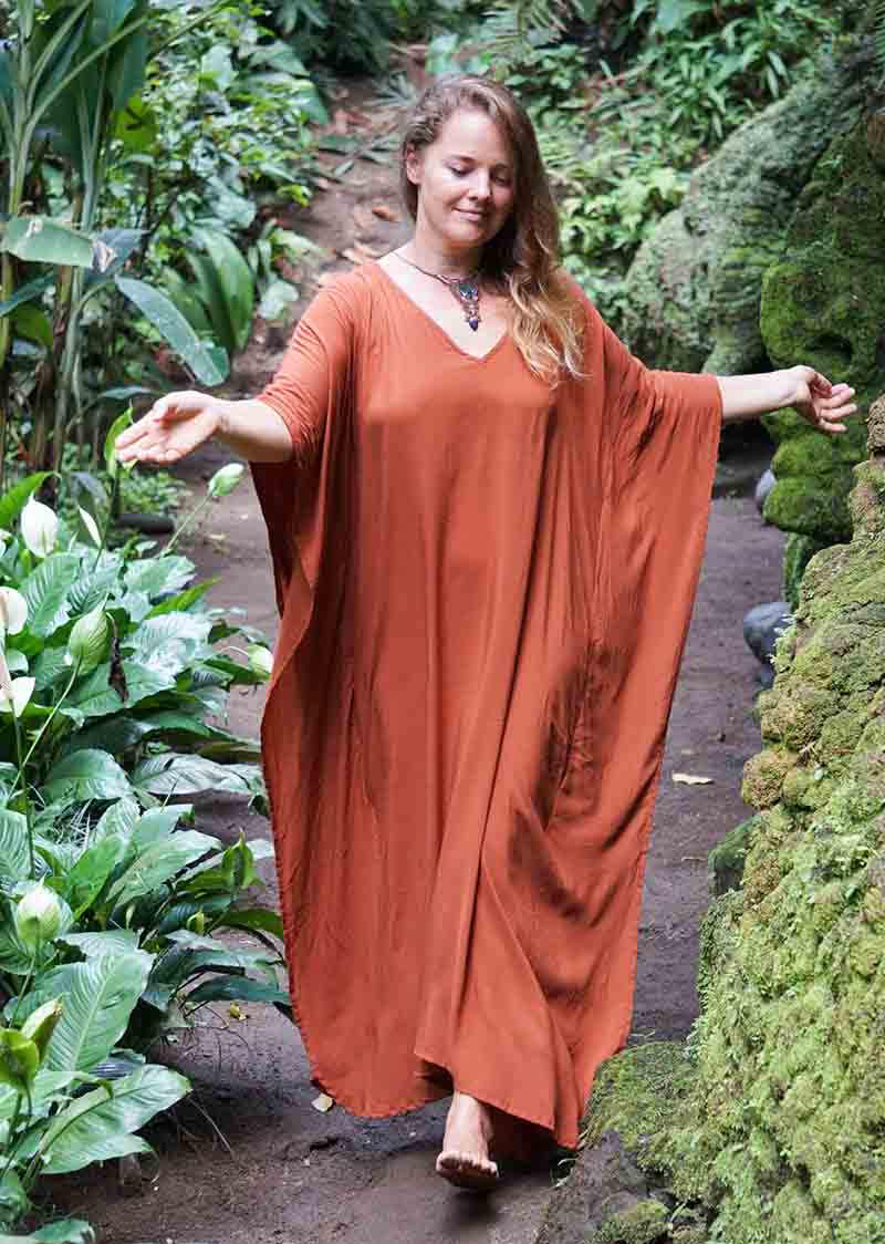 Woman in a rust-colored dress standing in a lush, green outdoor setting.