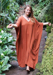 Woman in a rust-colored dress standing in a lush, green outdoor setting.