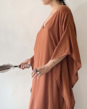 Person wearing a brown dress holding a feathered object against a plain background