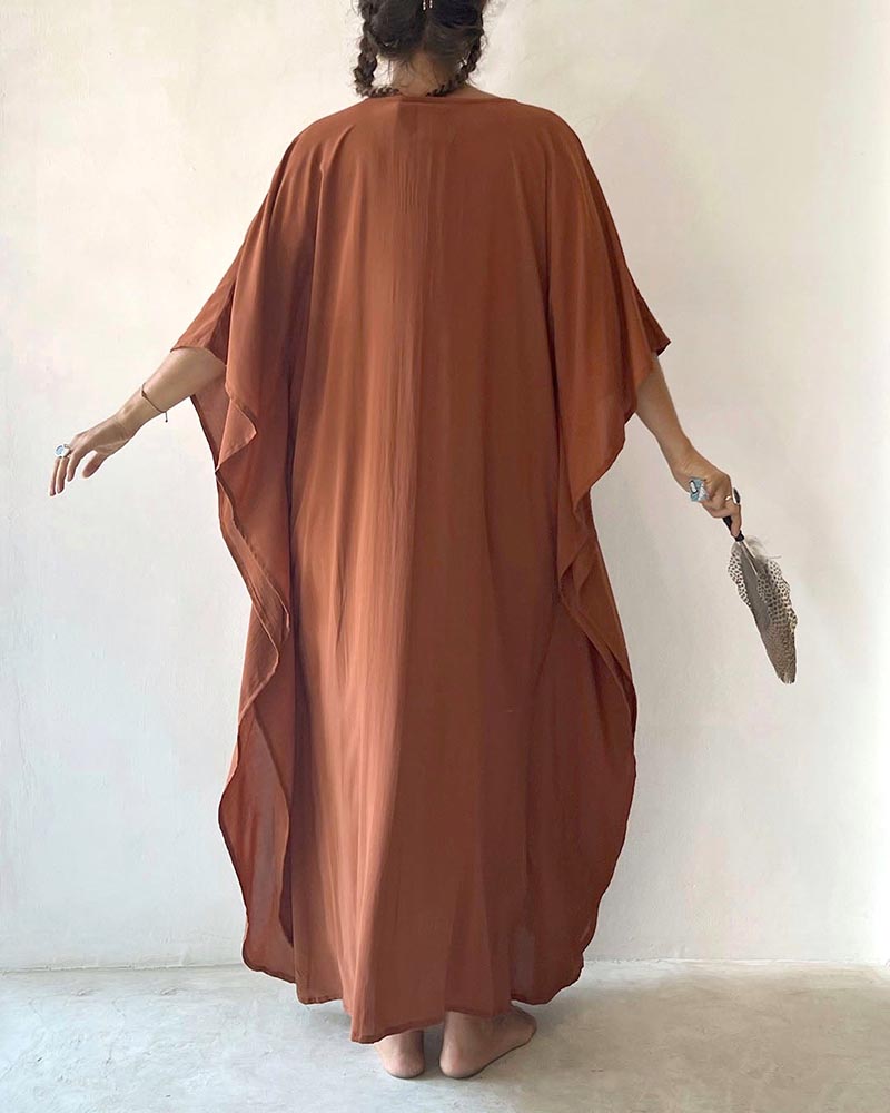 Person wearing a long, flowing brown dress holding a clutch against a plain background