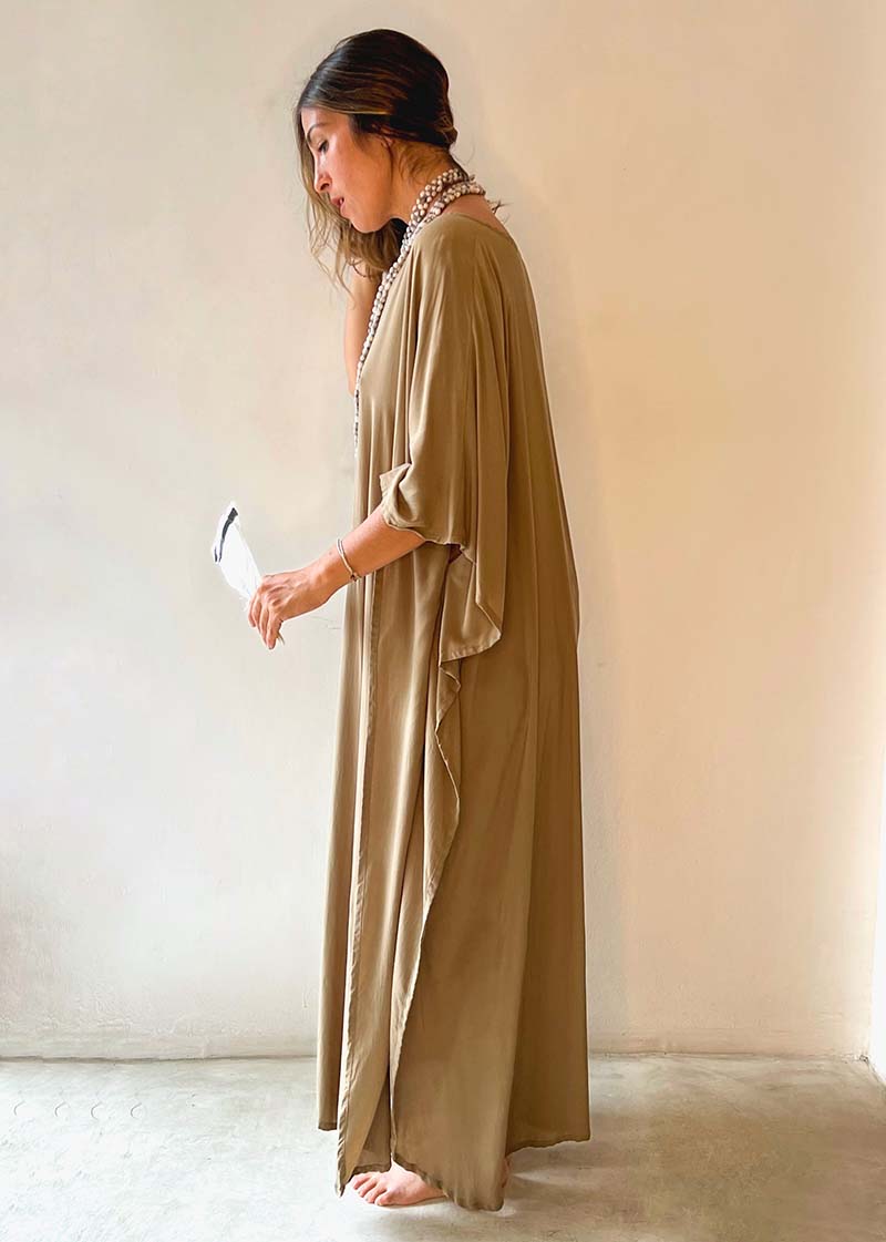 Woman wearing a long beige dress against a plain background