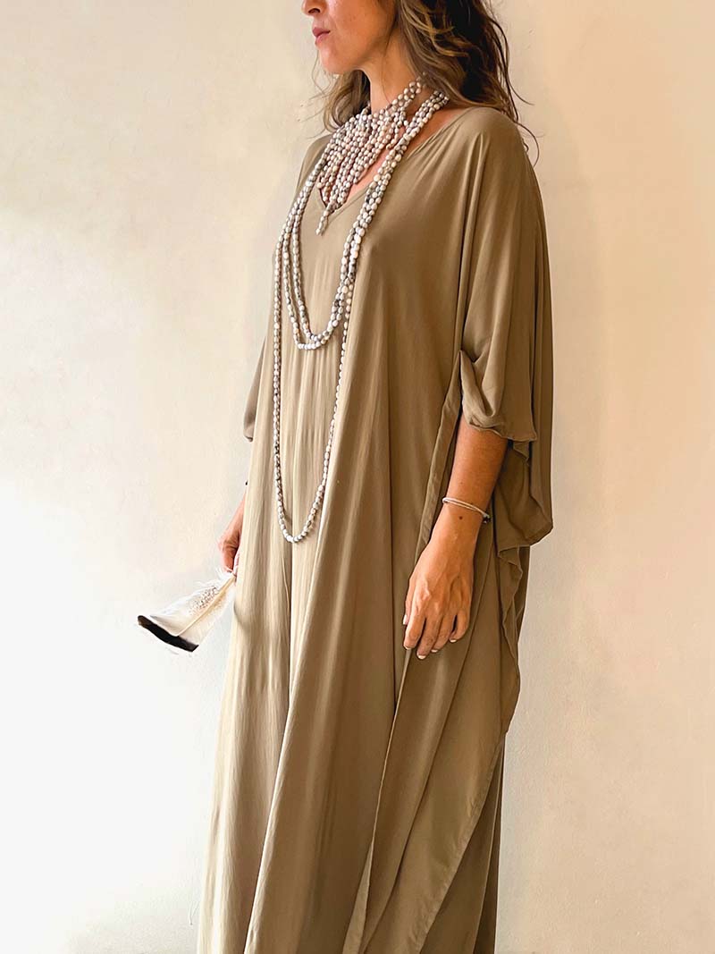 Woman wearing a long olive green dress with a pearl necklace against a beige background