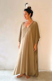 Woman wearing a long, light brown dress against a plain background