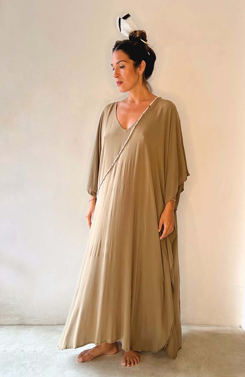 Woman wearing a long, light brown dress against a plain background