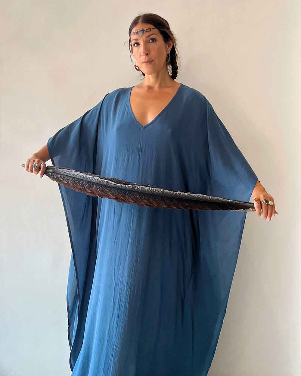 Woman wearing a blue dress holding a large black object against a plain background