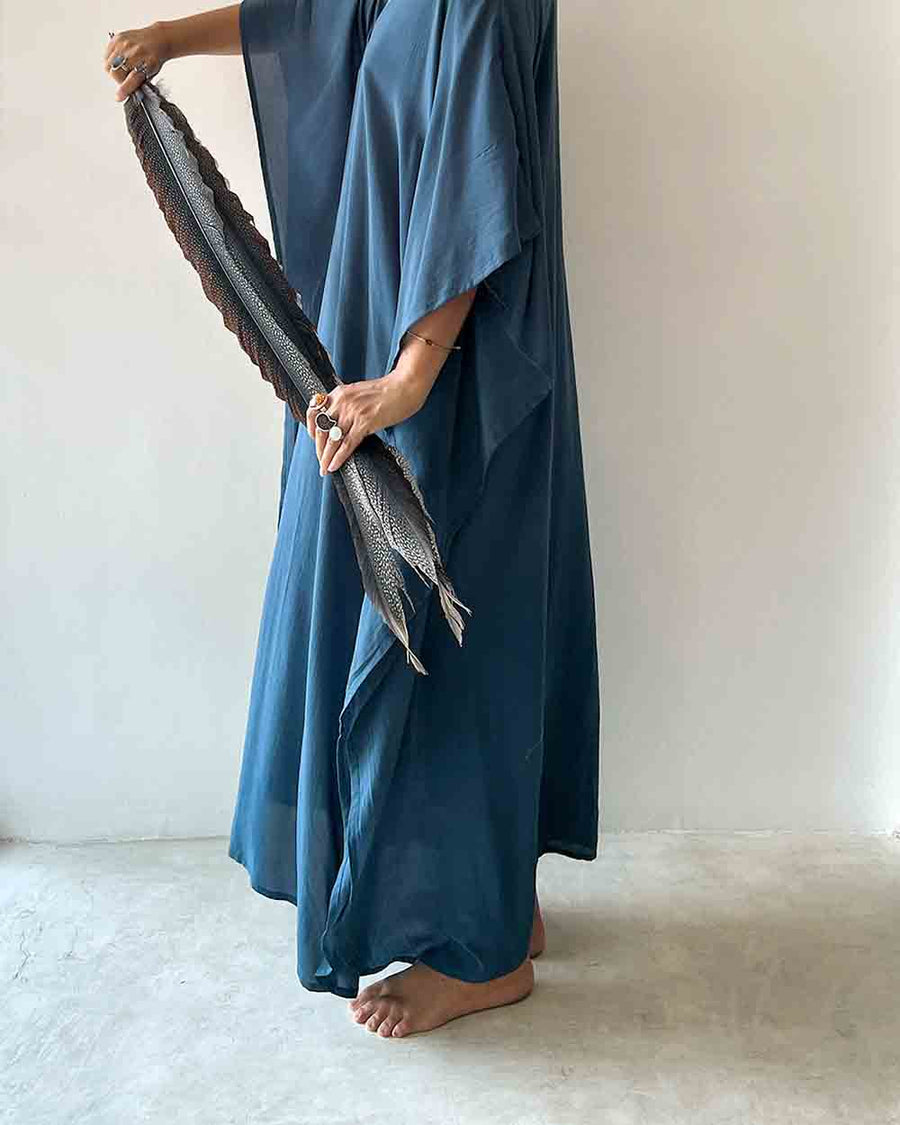 Person wearing a long blue dress holding a textured black and gray scarf against a plain background