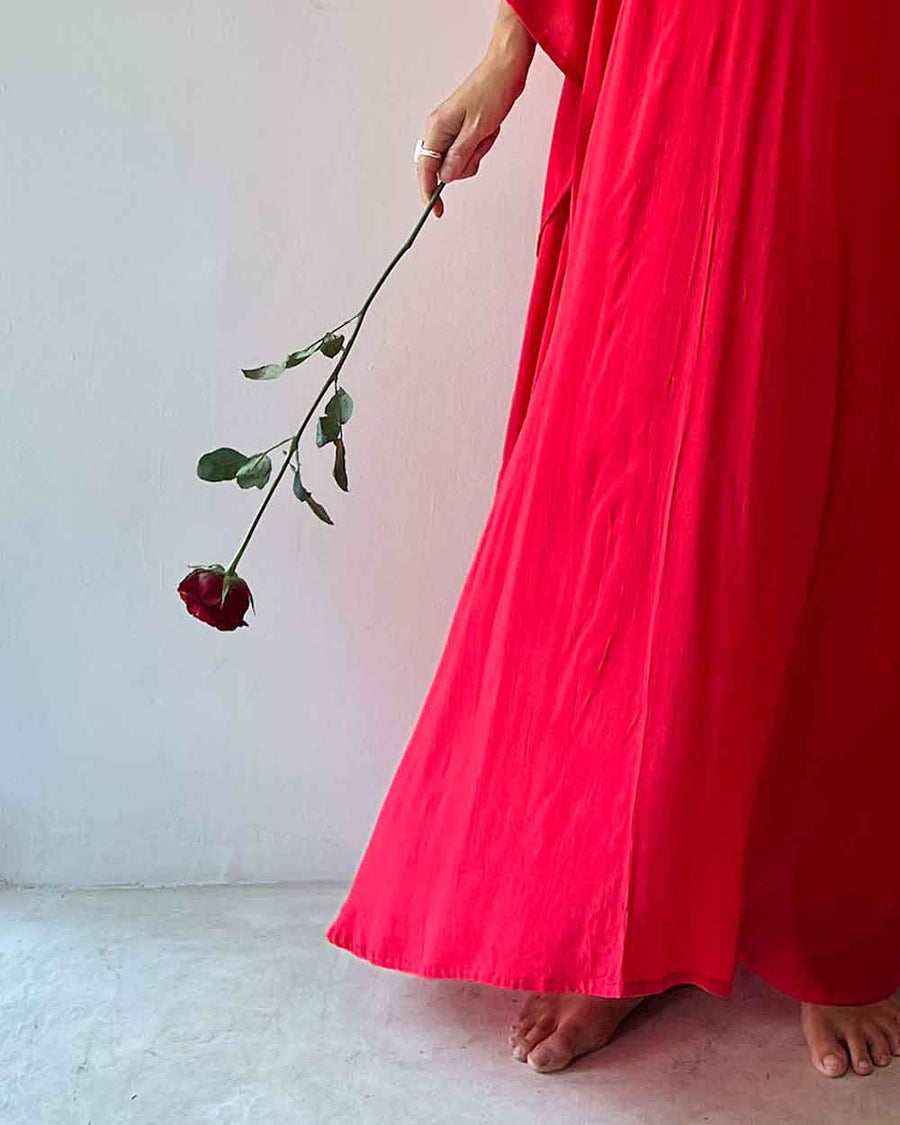 Person wearing a bright red dress holding a wilting red rose against a white background