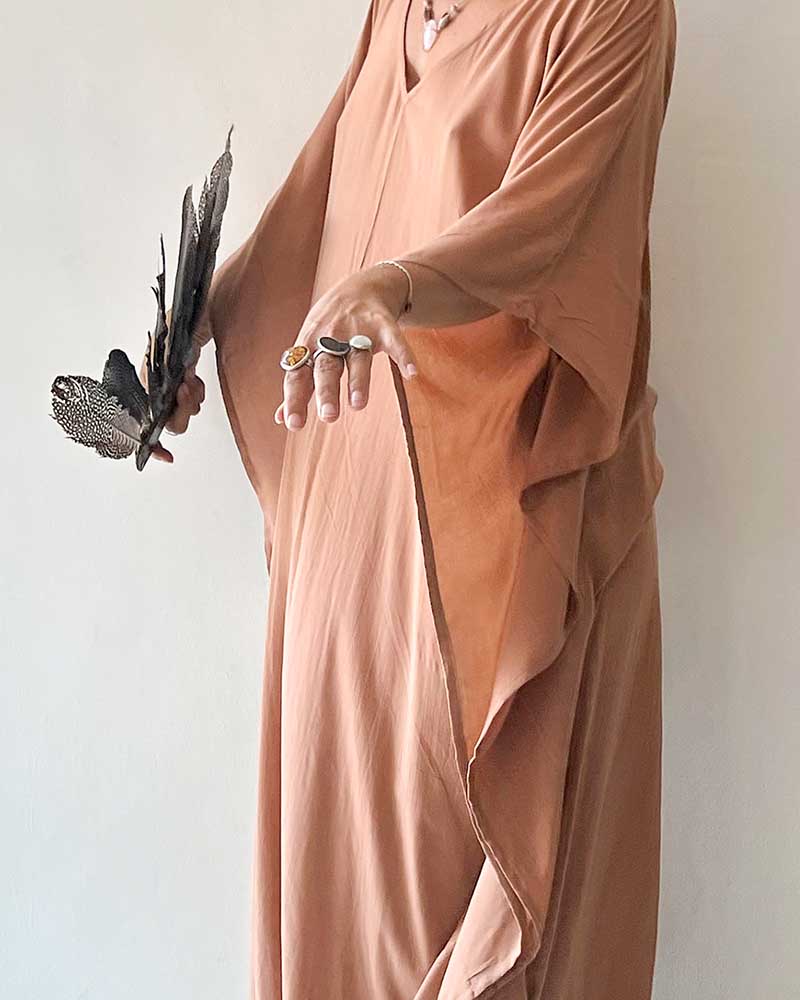 Person wearing a long, light brown garment holding feathers against a plain background