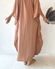 Person wearing a long, flowing brown dress holding a black clutch against a white background