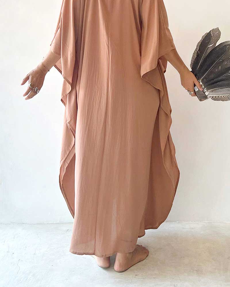 Person wearing a long, flowing brown dress holding a black clutch against a white background