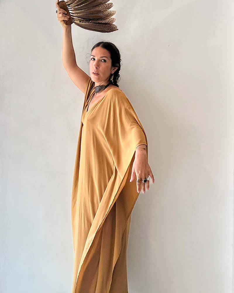 Woman in a mustard yellow dress holding a woven basket against a plain background
