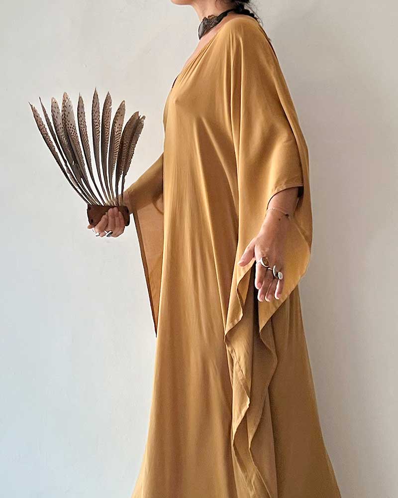 Person wearing a mustard yellow dress holding feathers against a plain background
