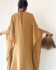Person wearing a mustard yellow dress holding a textured bag against a white background