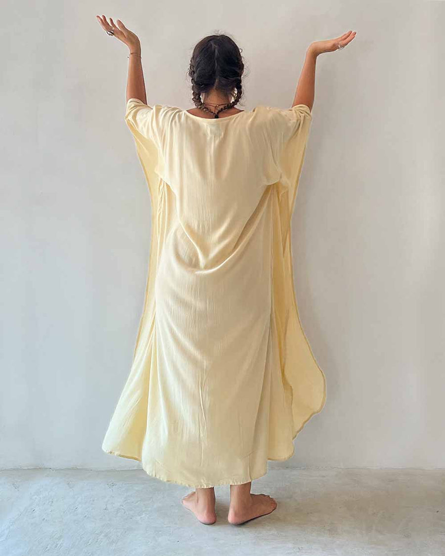 Person wearing a yellow dress with wide sleeves against a plain background