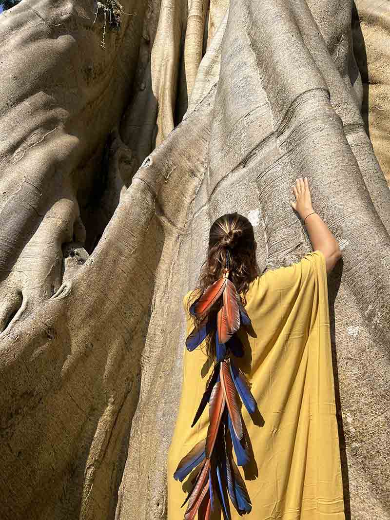 Woman in a yellow dress with colorful accents standing next to a large stone statue.
