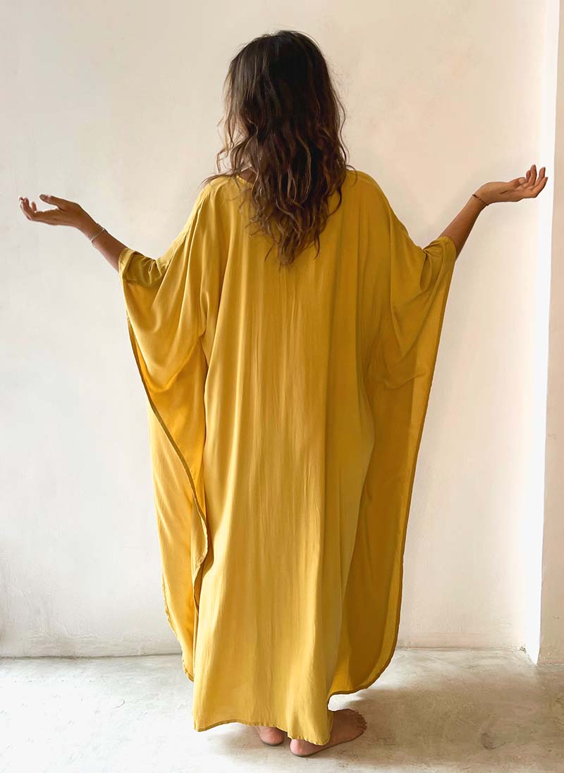 Woman wearing a yellow dress with her back to the camera against a white wall.
