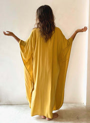 Woman wearing a yellow dress with her back to the camera against a white wall.
