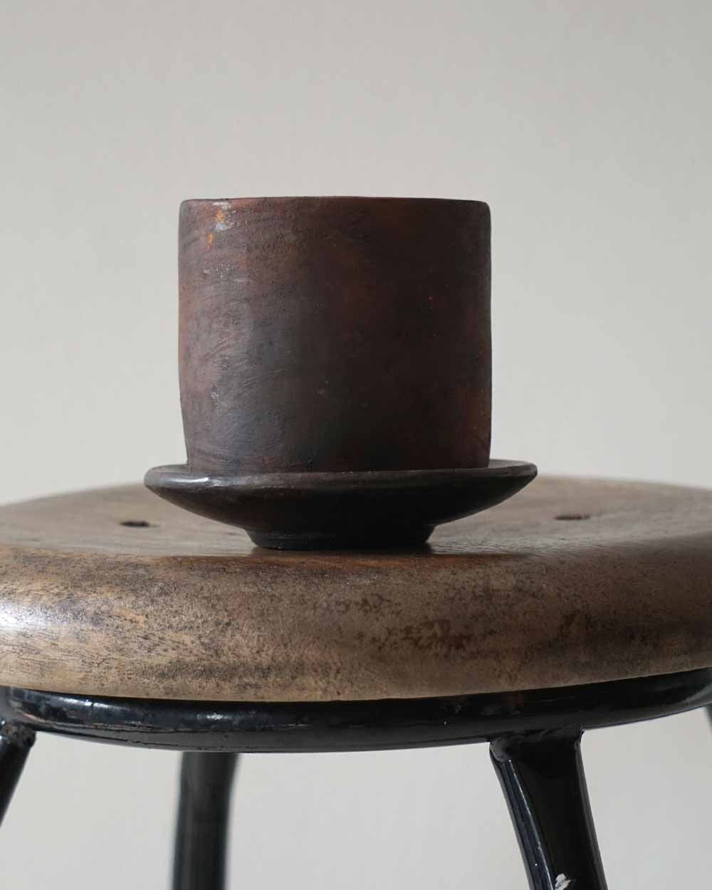 Brown ceramic cup on a matching saucer on a wooden stool with a white background