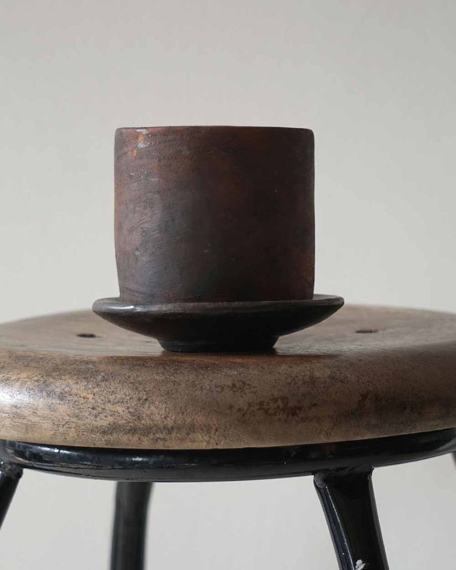 Brown ceramic cup on a matching saucer on a wooden stool with a white background