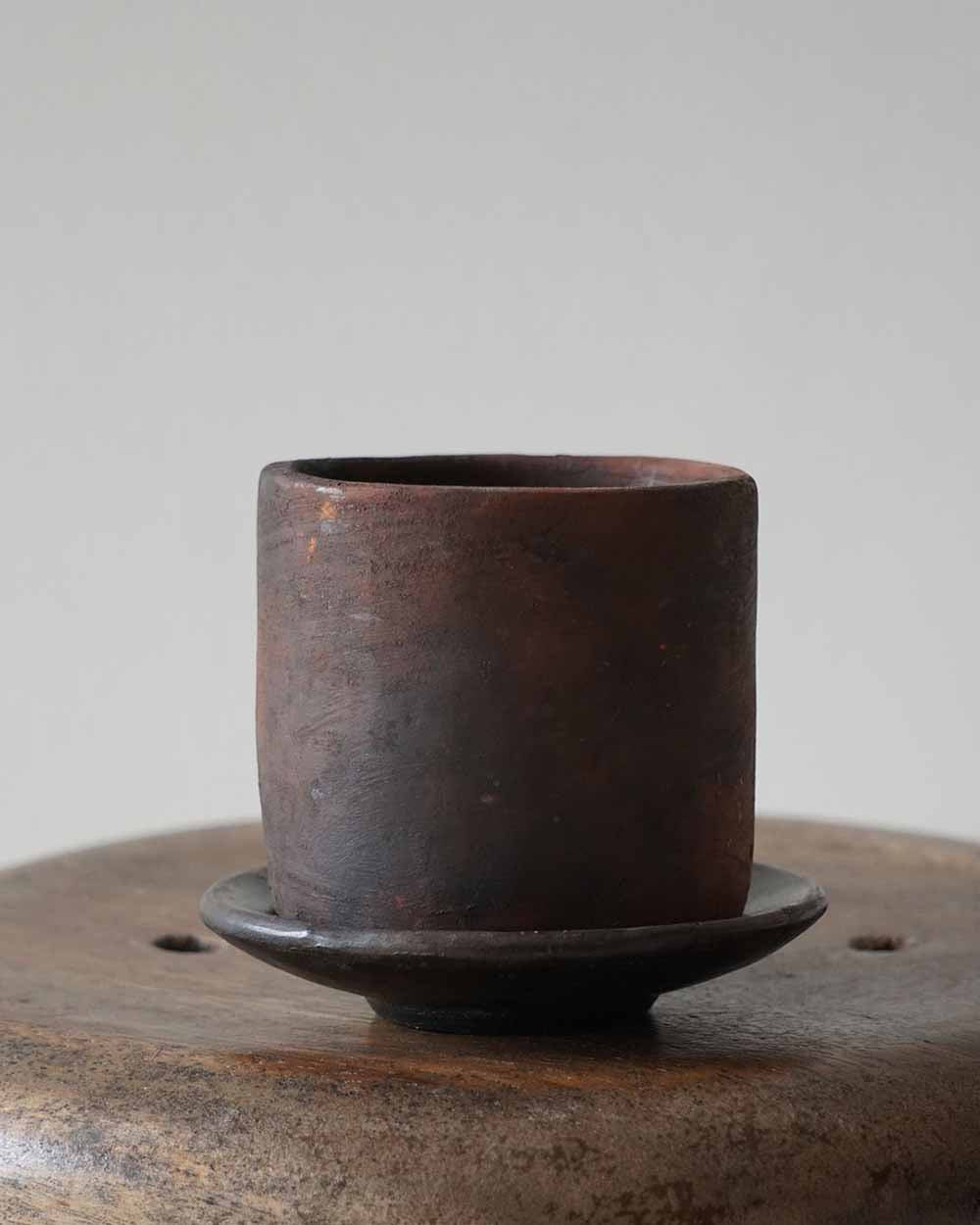 Rustic brown ceramic cup on a matching saucer against a neutral background