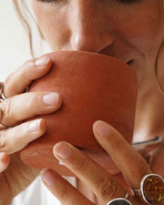 Person holding a terracotta mug close to their face