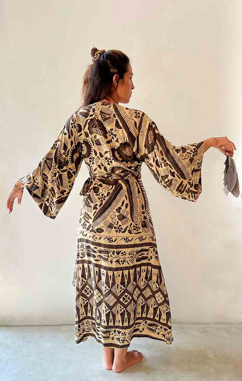 Woman wearing a patterned dress holding a small bag against a plain background