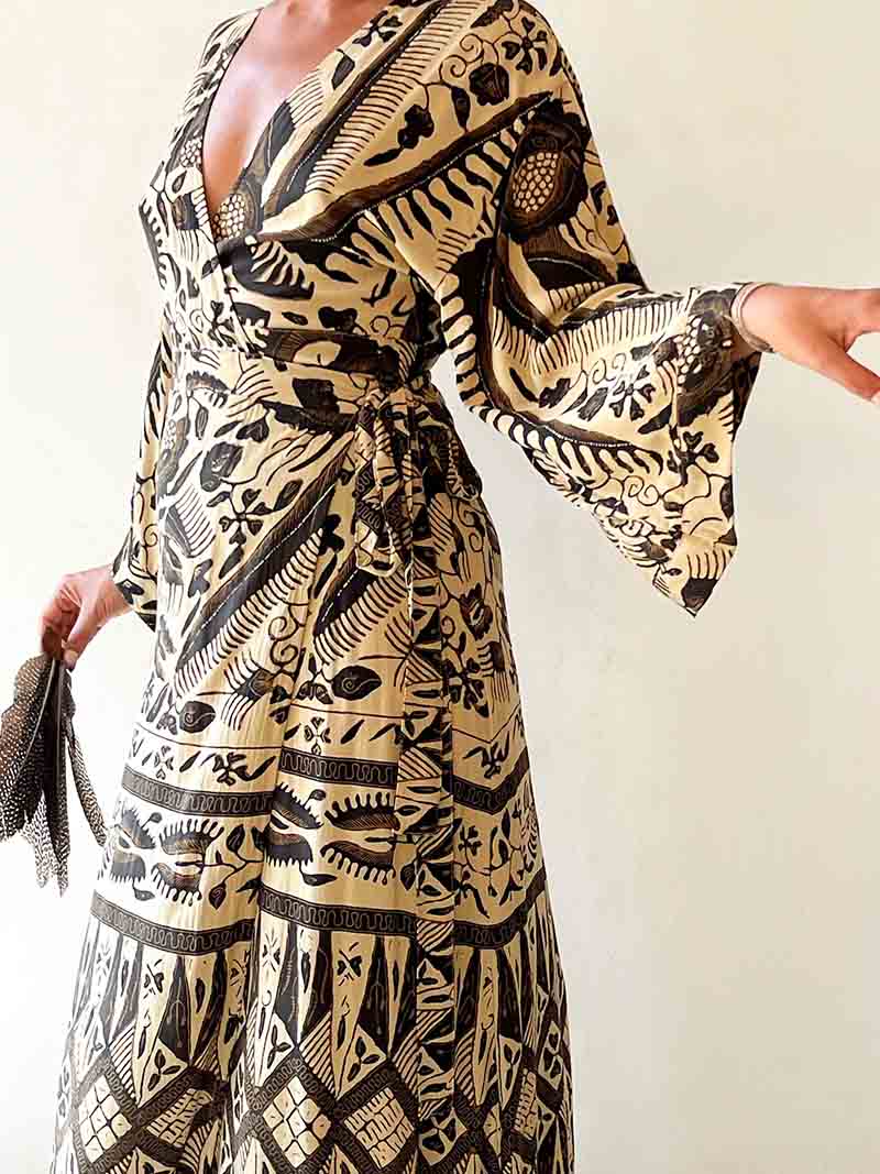 Woman wearing a black and gold patterned dress with bell sleeves against a white background