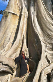 Person posing inside a large tree with a blue sky background